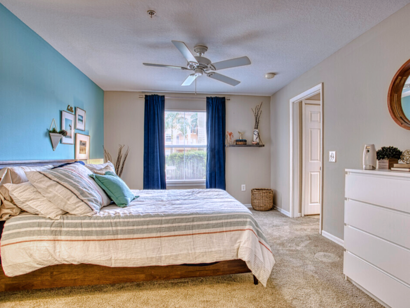 This image is a master bedroom featuring patterned pillows with bright accents that are welcoming. It also showcases the Ceiling fans and wooden mirror.